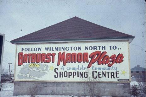 Sign for Bathurst Manor Plaza, a shopping center, with map and text against a snowy sky.