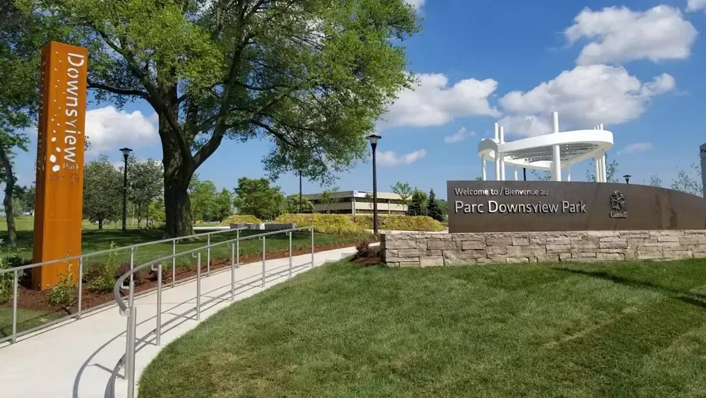 Signage for Downsview Park, with a path leading towards a gazebo under a blue sky.