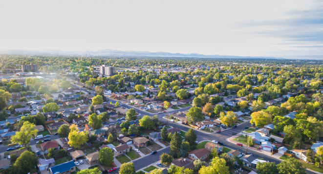 Aerial view of a suburban neighborhood with houses, trees, and roads under a clear sky.