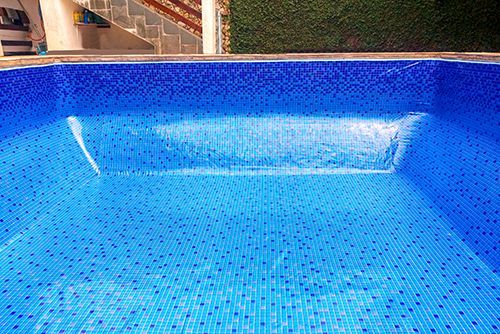 A large swimming pool with blue tiles and stairs in the background.