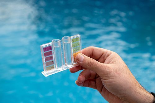 A person is holding a test tube in front of a swimming pool.