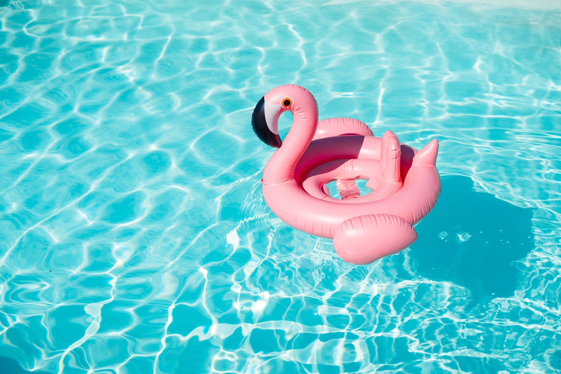 Flamingo float drifts on bright blue water under sunny sky.