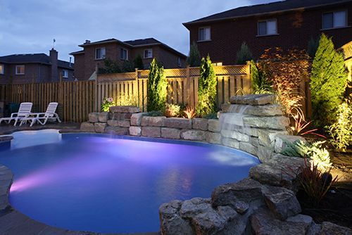 A large swimming pool is lit up at night with purple lights.