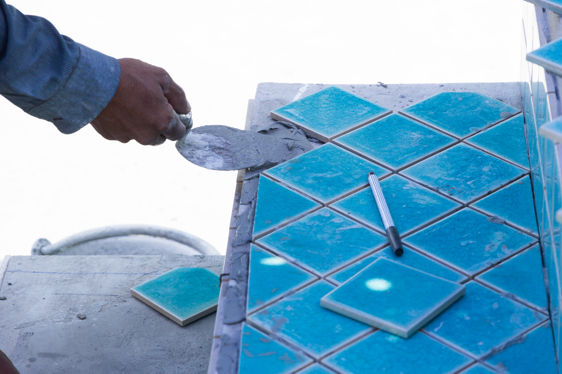 Commercial swimming pool contractor places pool tiles on a surface, under the sun.