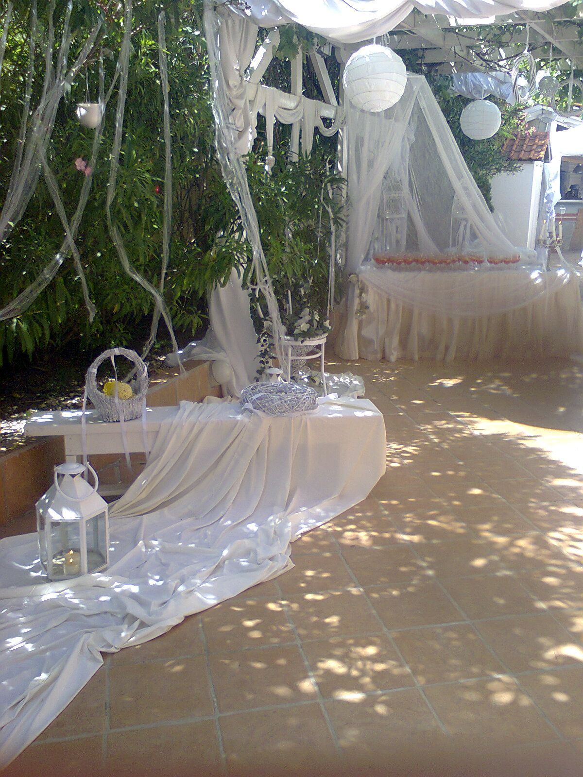 A table with white cloth and lanterns on it is sitting under a canopy.