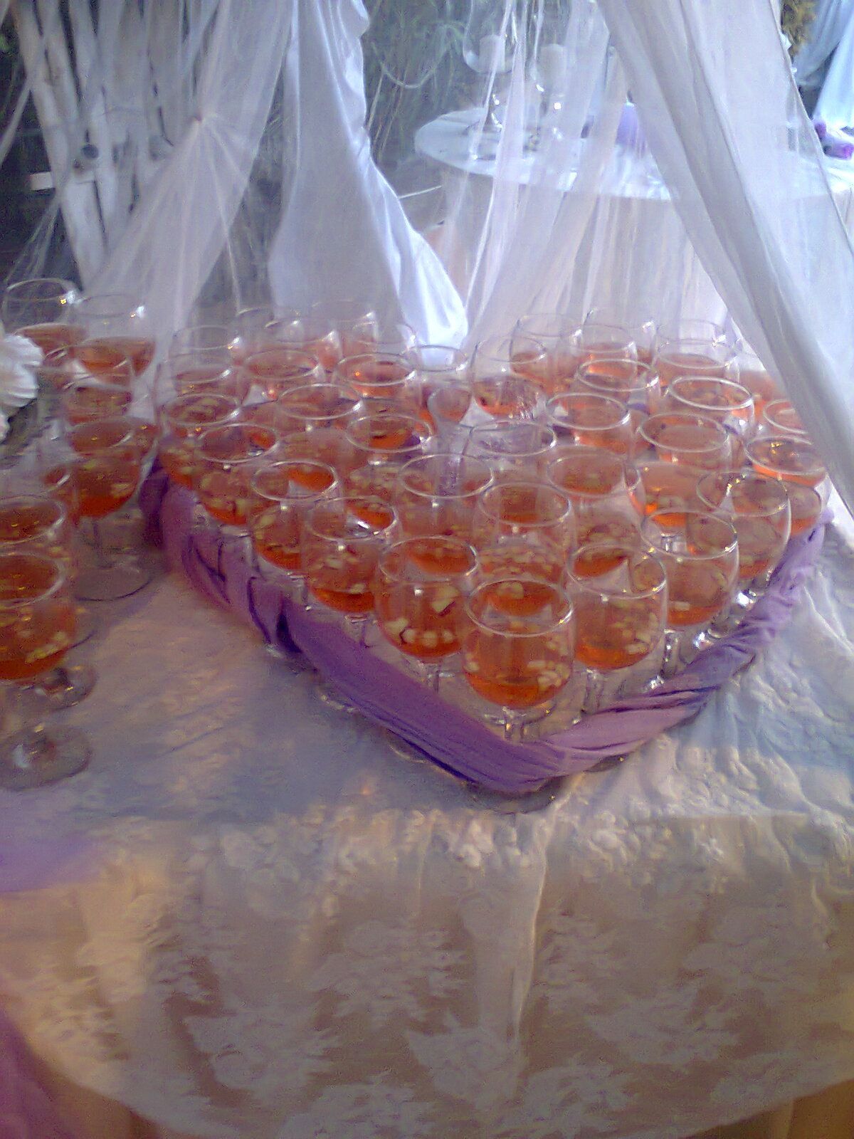 A heart shaped basket filled with shot glasses of wine on a table.