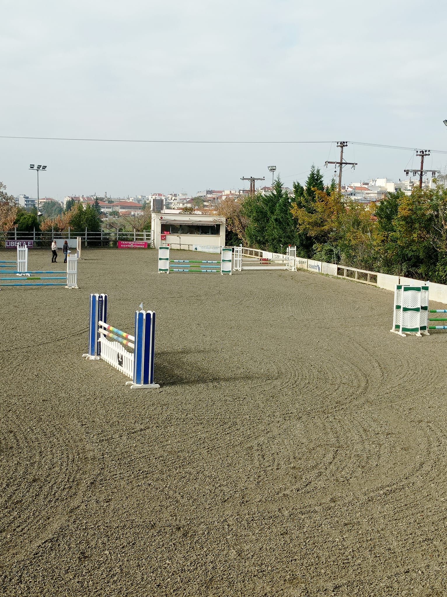 A dirt field with jumping fences and trees in the background.