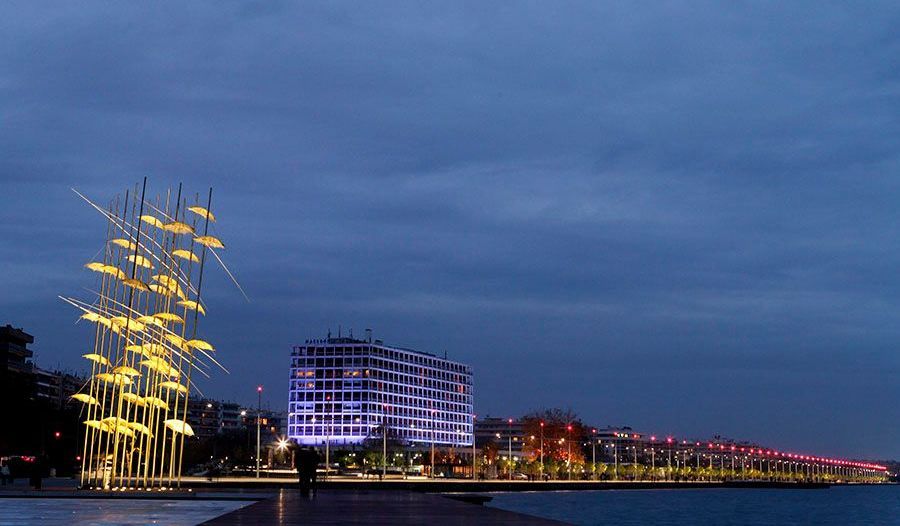A statue of a sailboat is lit up at night next to a body of water.
