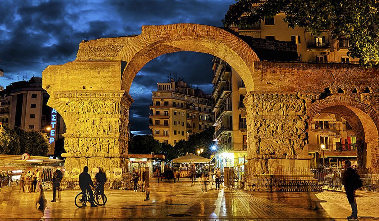 A group of people are standing in front of a stone archway at night.