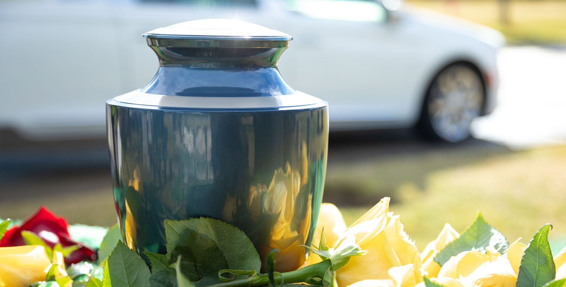 A blue urn sitting on top of a table next to yellow roses.