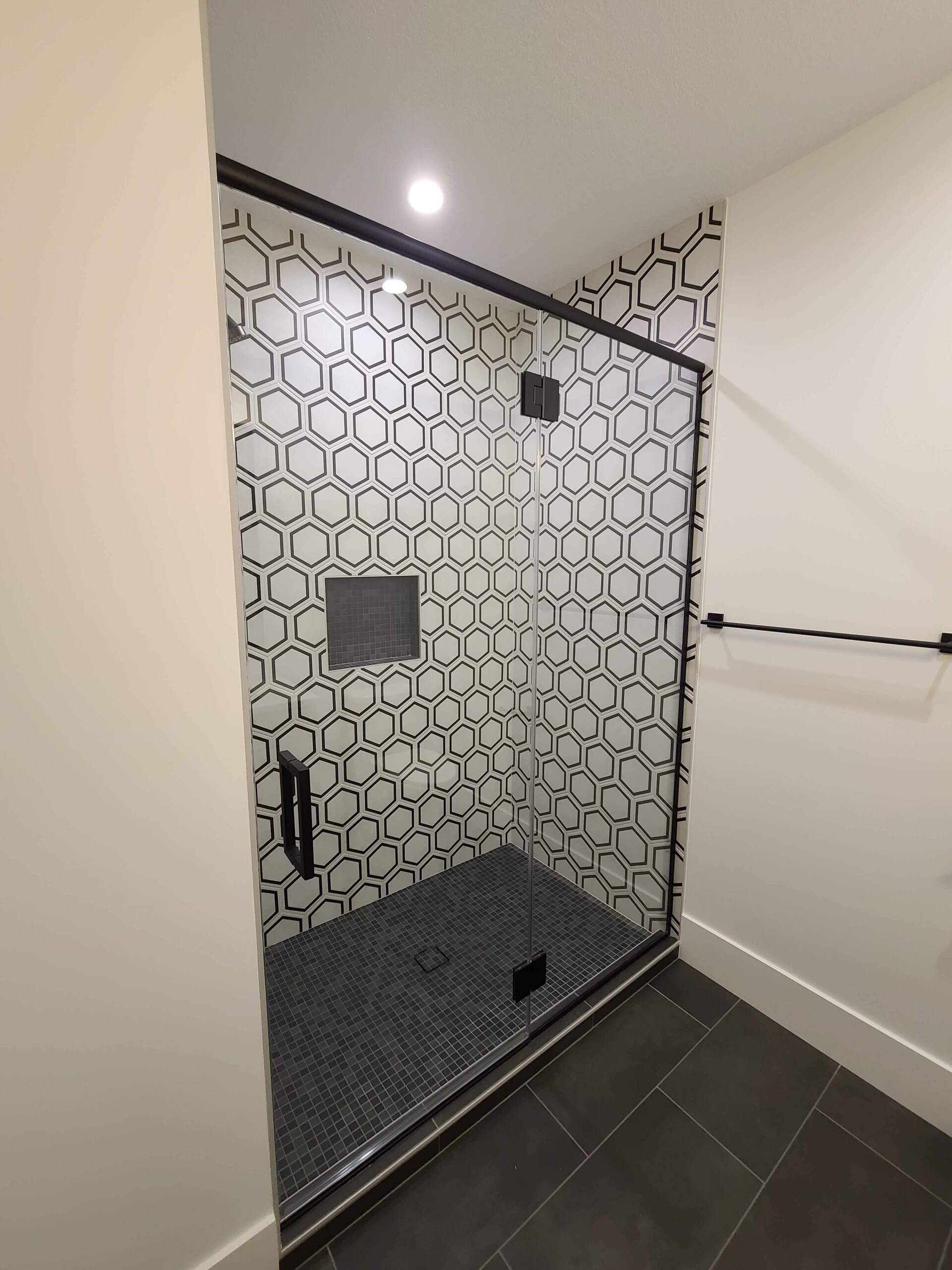A bathroom with a walk in shower with a black and white tile wall.