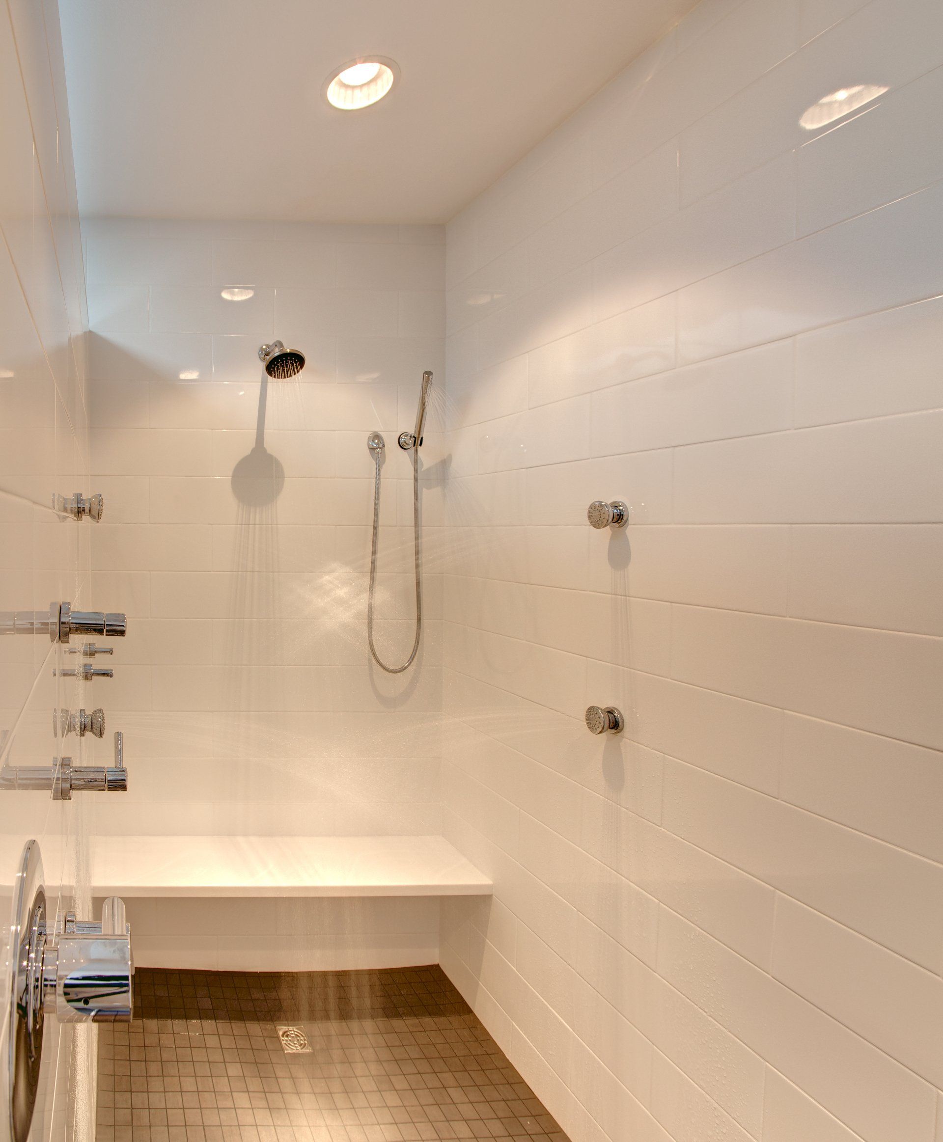 A bathroom with white tiles and a shower with a bench.