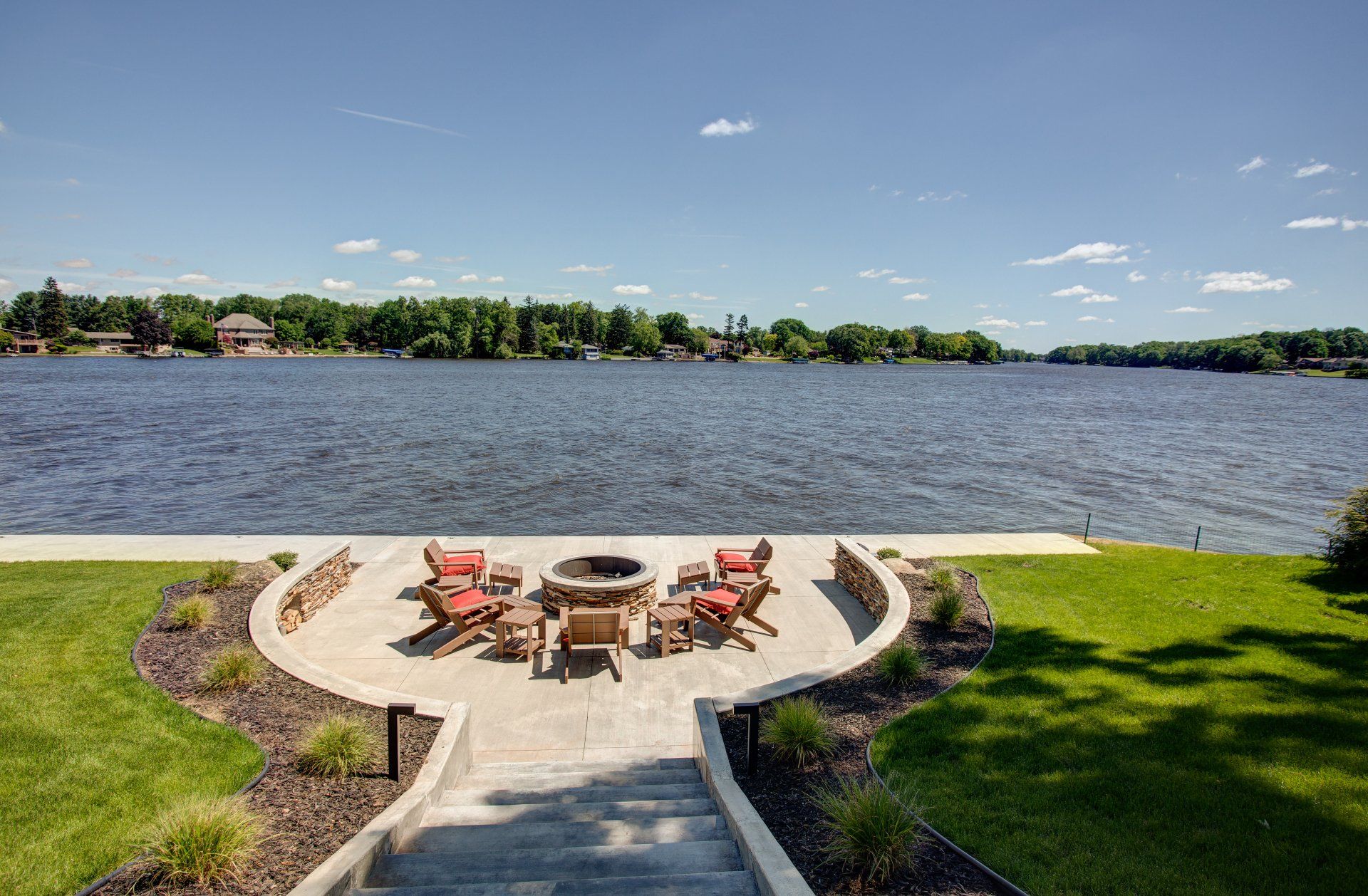 A patio with a fire pit and chairs overlooking a lake.