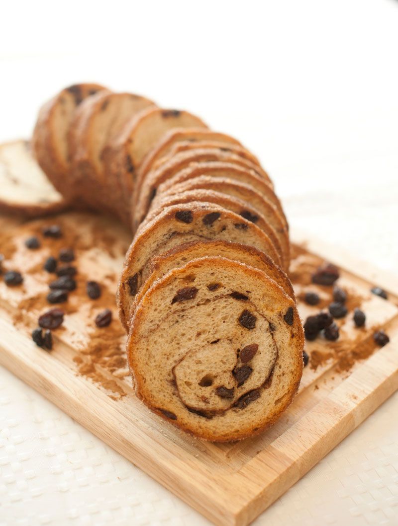 A loaf of raisin bread is sitting on a wooden cutting board.