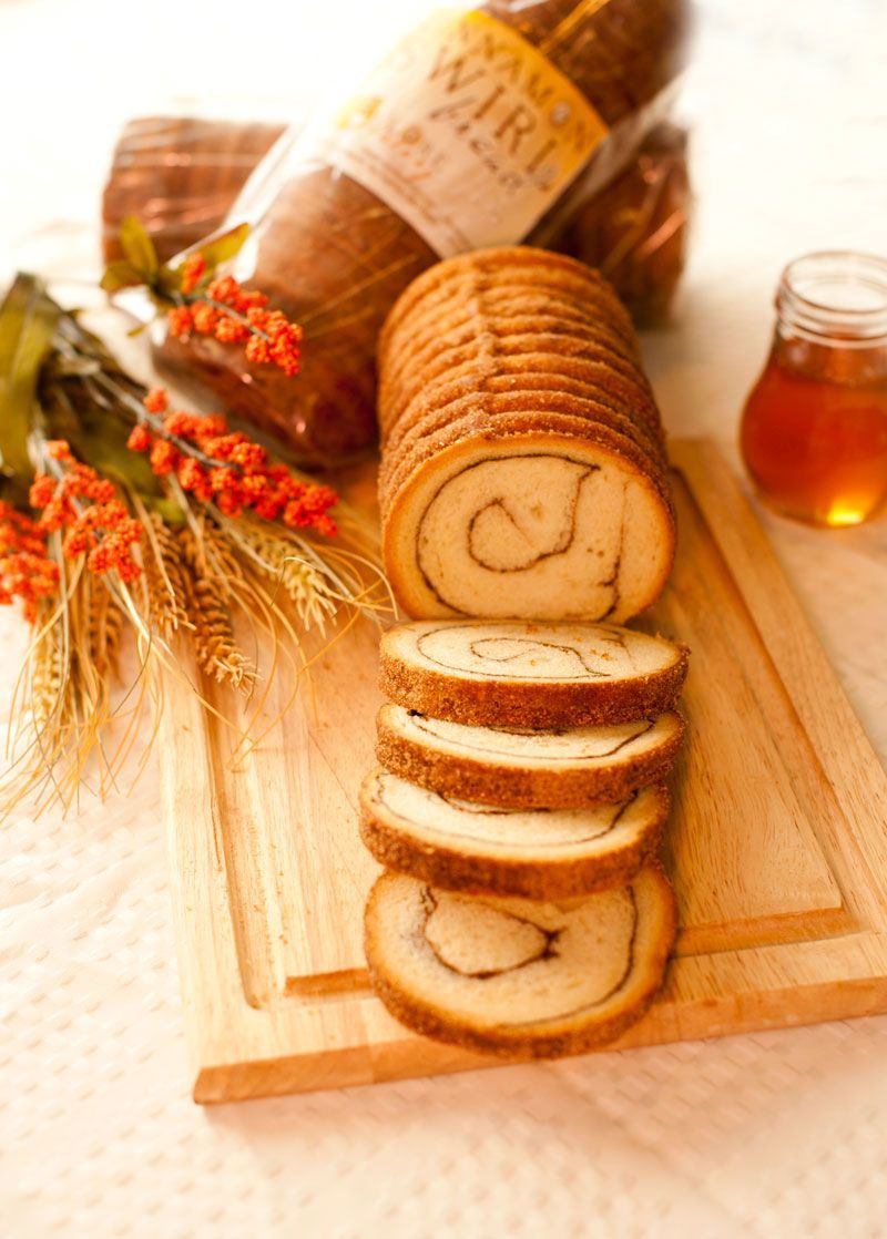A loaf of bread is sitting on a wooden cutting board next to a jar of honey.