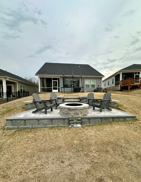 Fire pit with seating on a tiered patio in a backyard, with a house in the background.