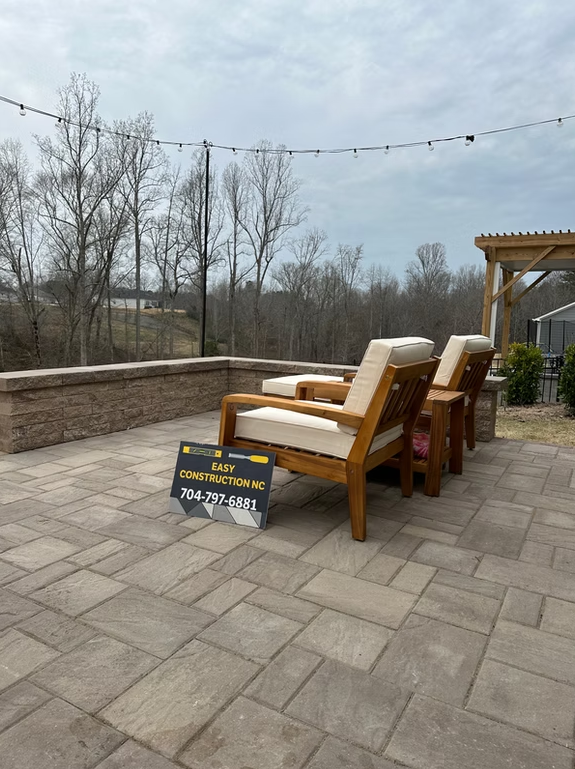 Two wooden outdoor chairs with white cushions on a paved patio, cloudy sky.