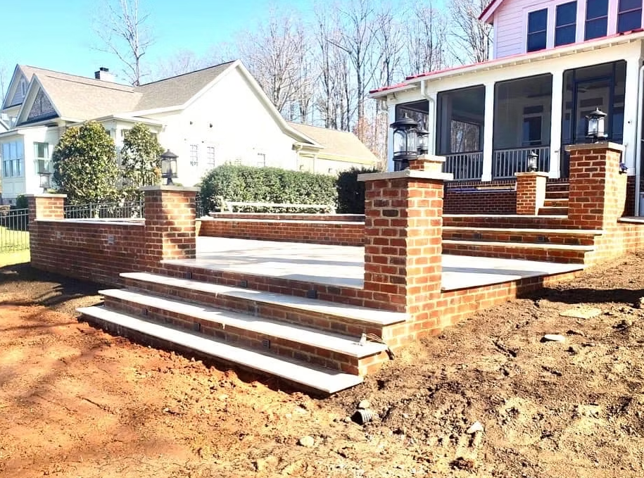 Brick patio with steps, pillars, and a porch in a residential setting.