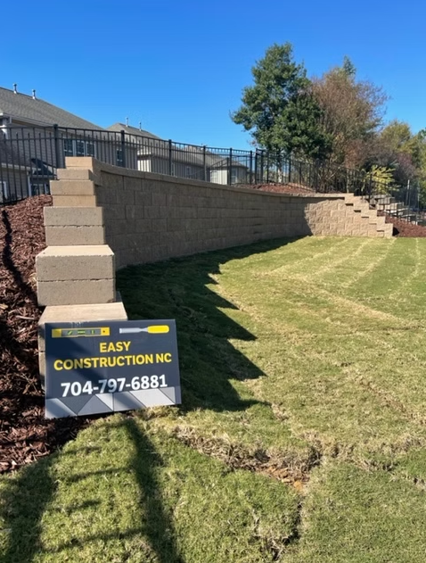 Retaining wall with steps in a backyard, beside a lawn. Sign for