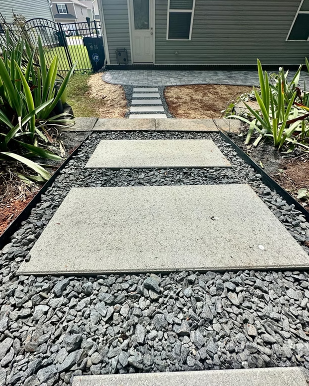 Concrete stepping stones in black gravel pathway leading to a house, with green plants on each side.