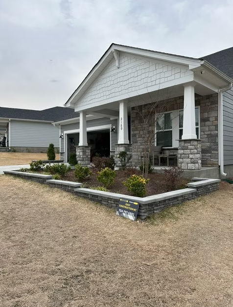 Stone-faced house with a porch and raised garden beds on a cloudy day.