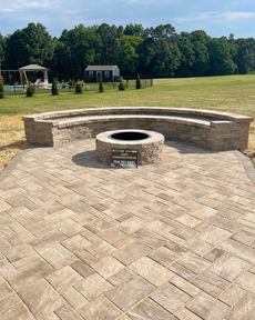 Stone patio with fire pit and curved seating area, trees in the background.