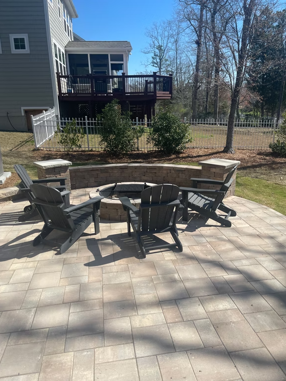 Outdoor patio with fire pit, Adirondack chairs, and house in background.