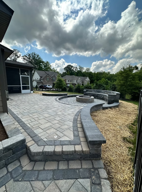 Stone patio with fire pit and seating, under a cloudy sky.