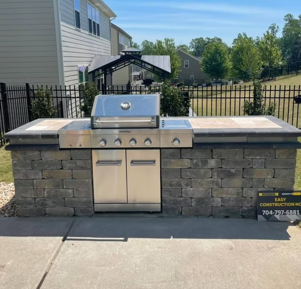 Outdoor grilling station with stainless steel grill, stone facade, and countertop.