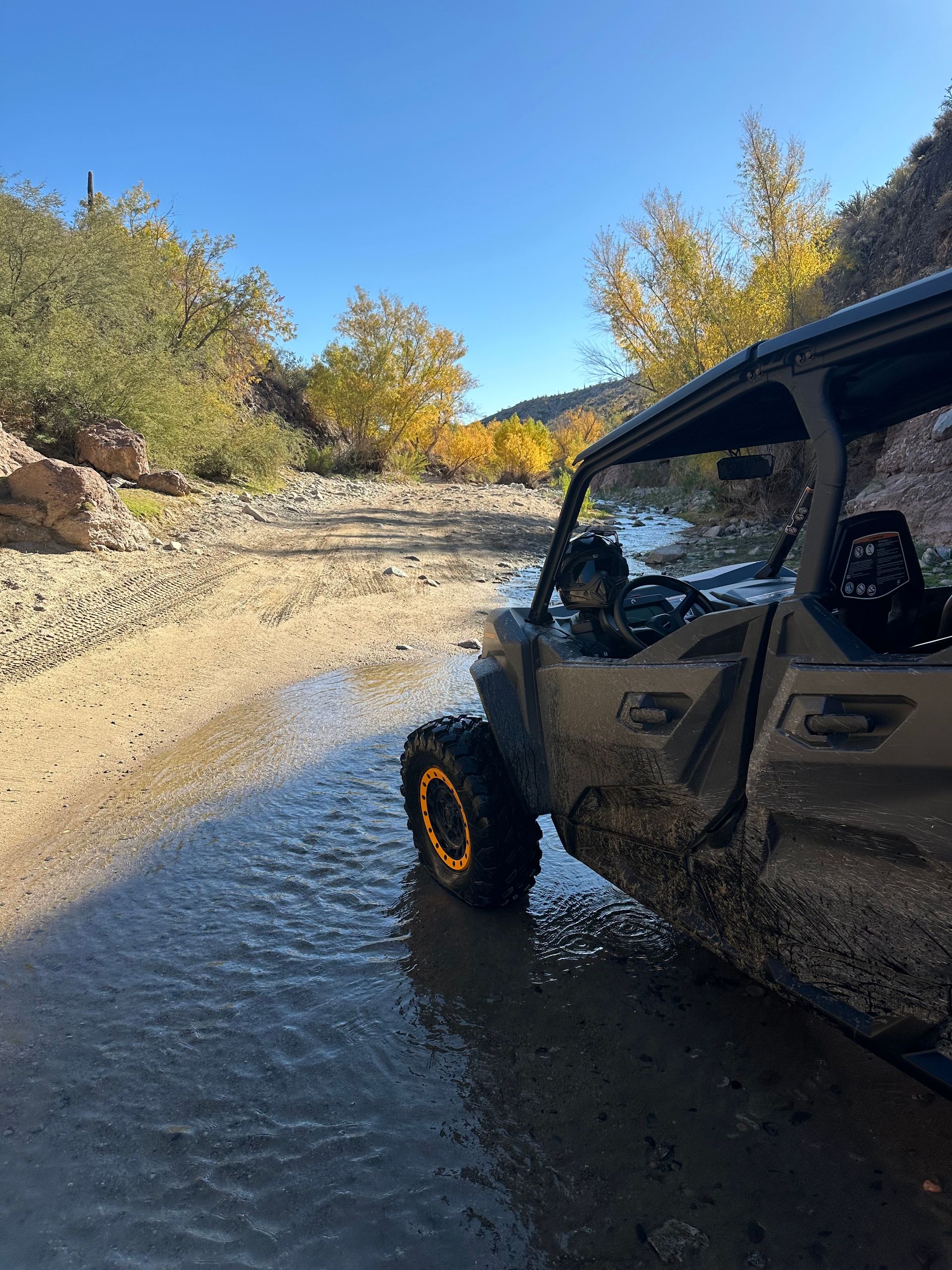 A muddy atv is driving through a muddy river.