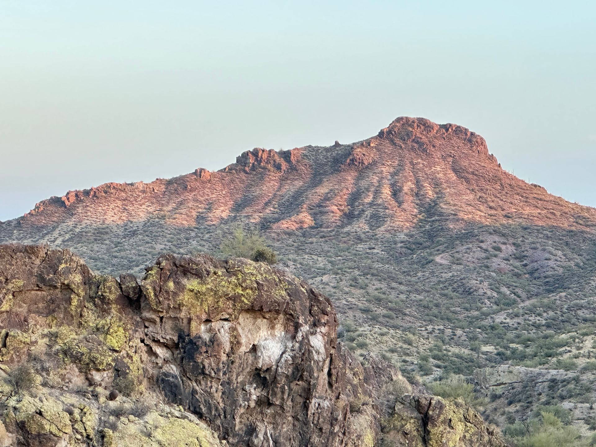 A mountain in the desert with a cliff in the foreground.