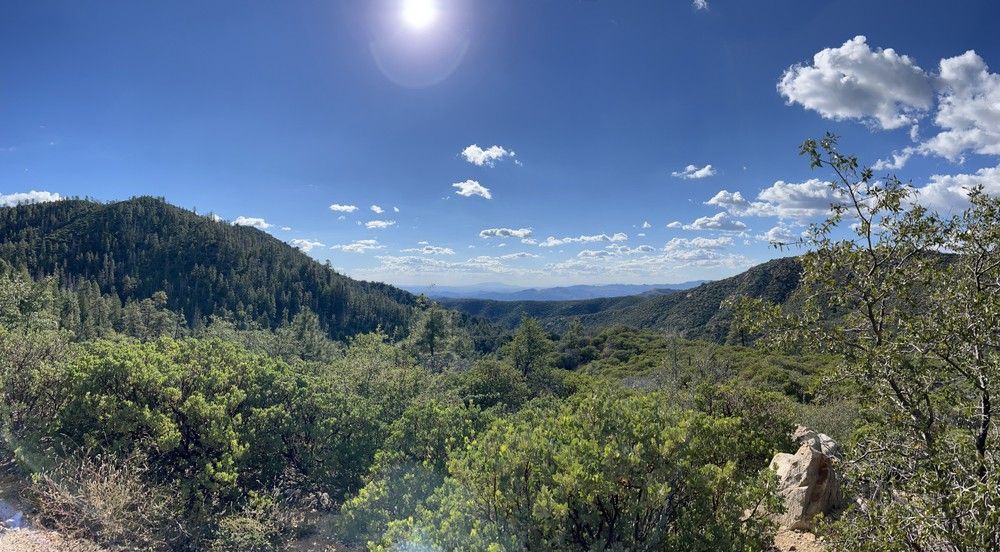 A view of a valley filled with trees and mountains with the sun shining through the clouds.