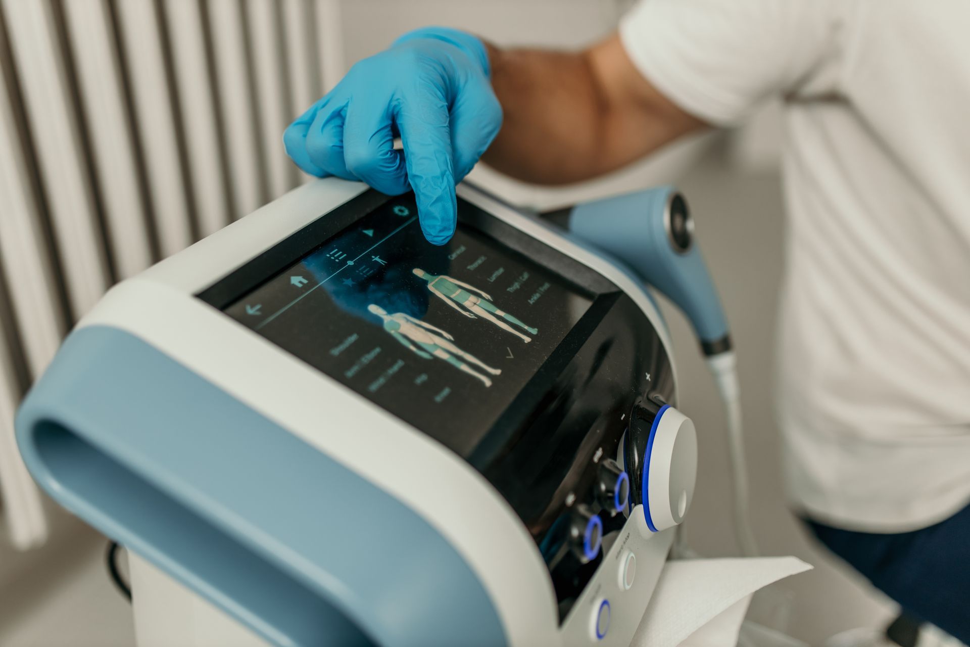 Person in blue glove points to a medical device's screen, showing body diagrams.