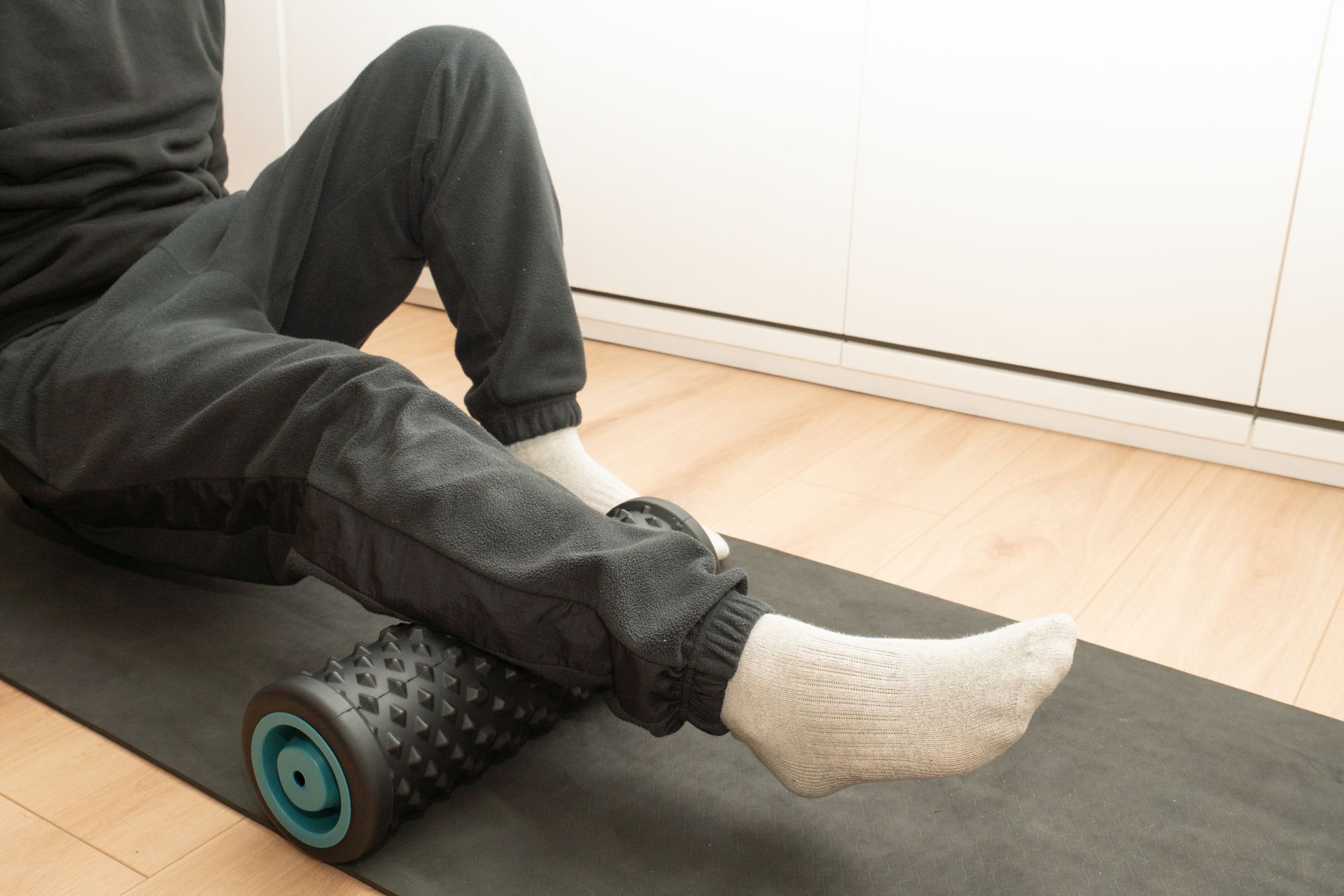 Person using a foam roller on the calf muscle on a mat. Indoors, natural light.