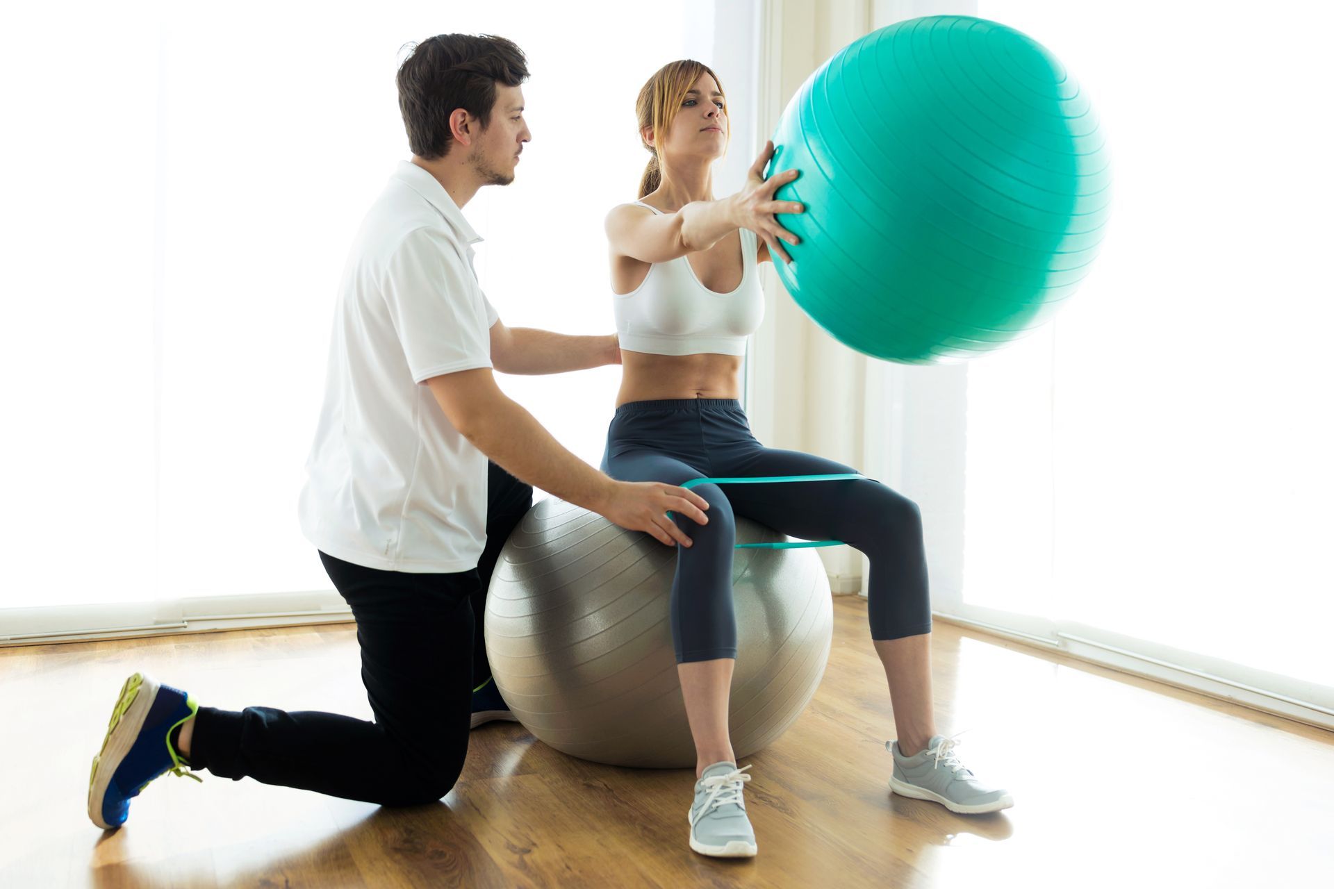 Man assisting woman exercising with stability ball and band.