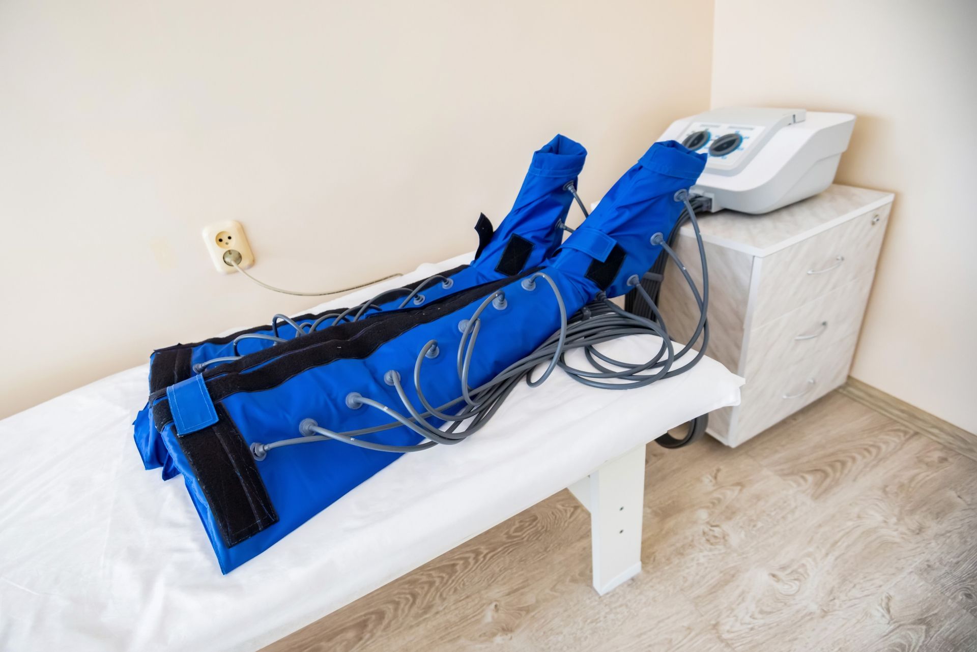 Blue pneumatic compression boots for lymphatic drainage therapy, resting on a medical examination table.