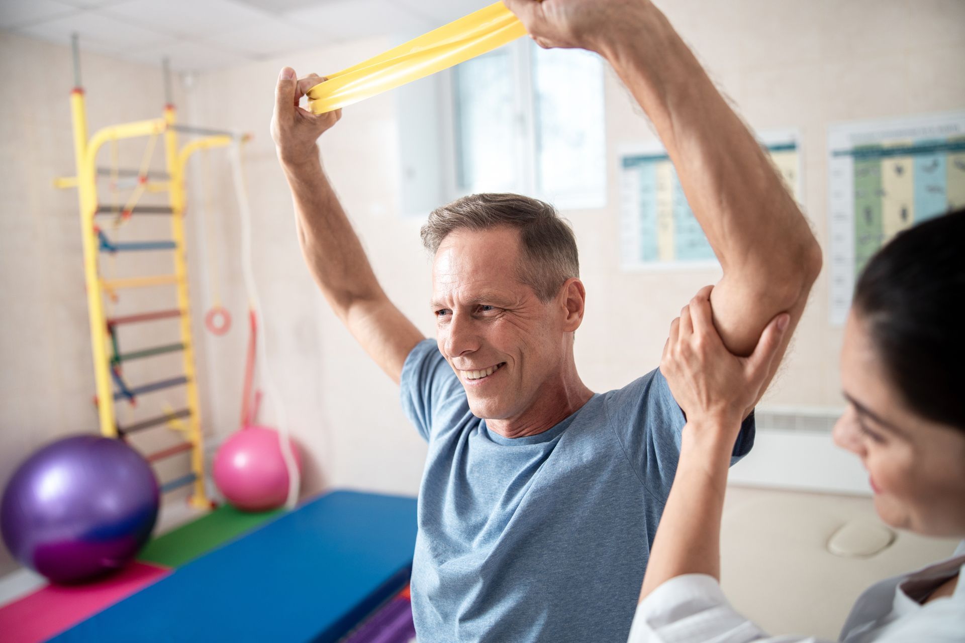 Man in therapy exercises arm with resistance band, assisted by therapist.