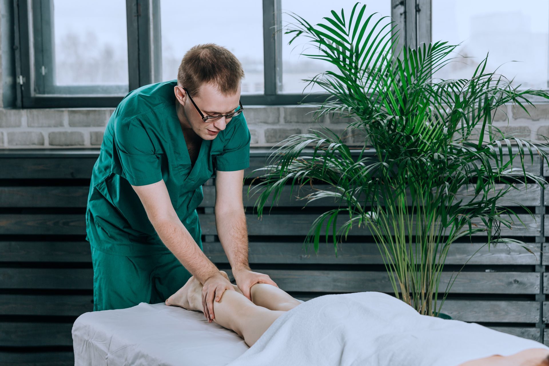 Massage therapist in green scrubs giving a leg massage on a massage table.