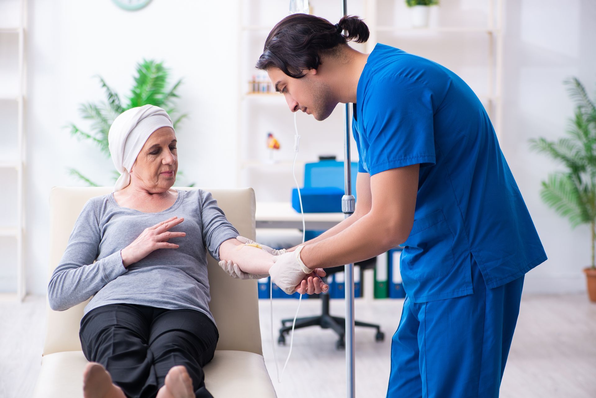 Nurse administering IV to a person with head covering, receiving treatment. Medical setting.