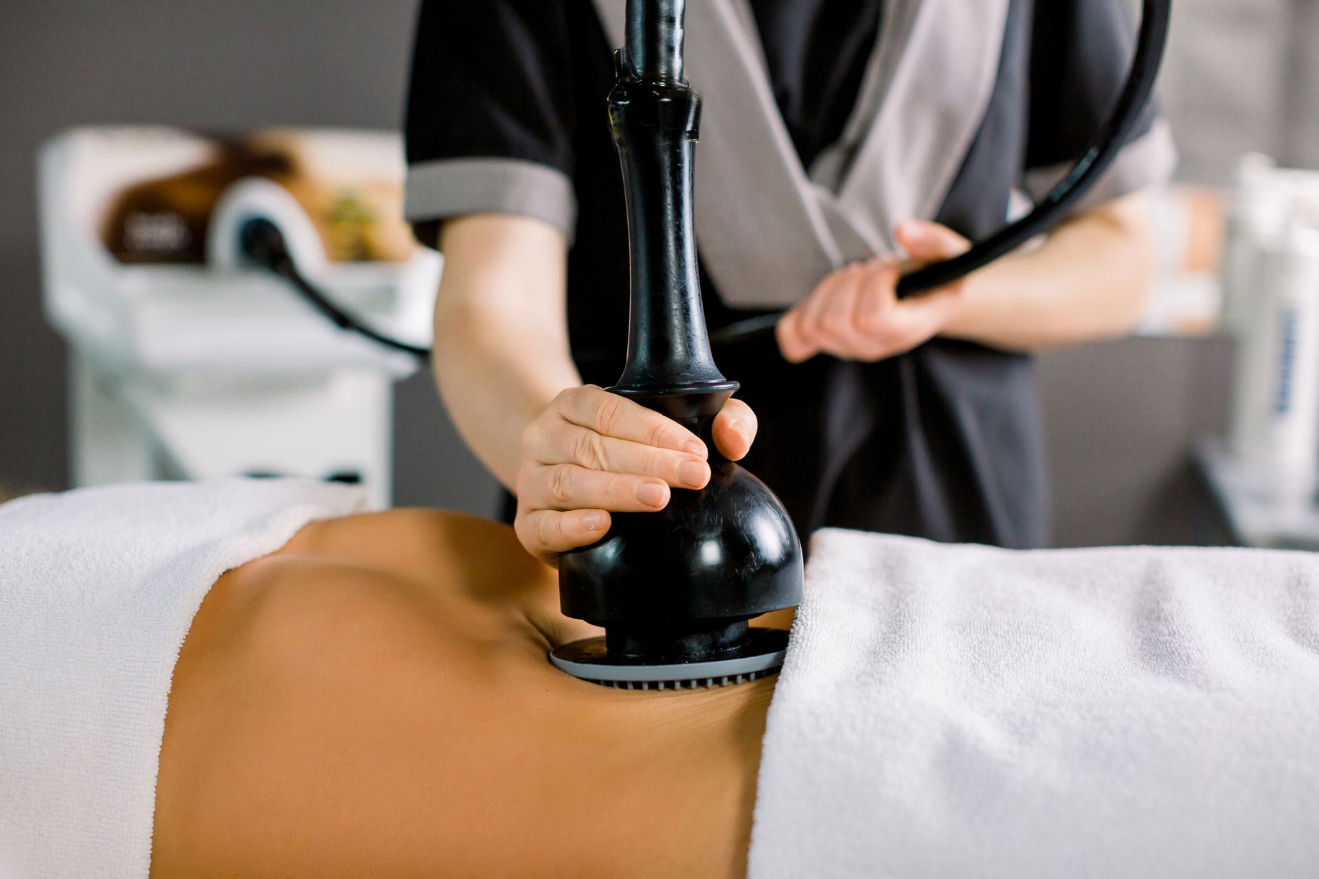 Person receiving stomach treatment with a black device in a spa setting.