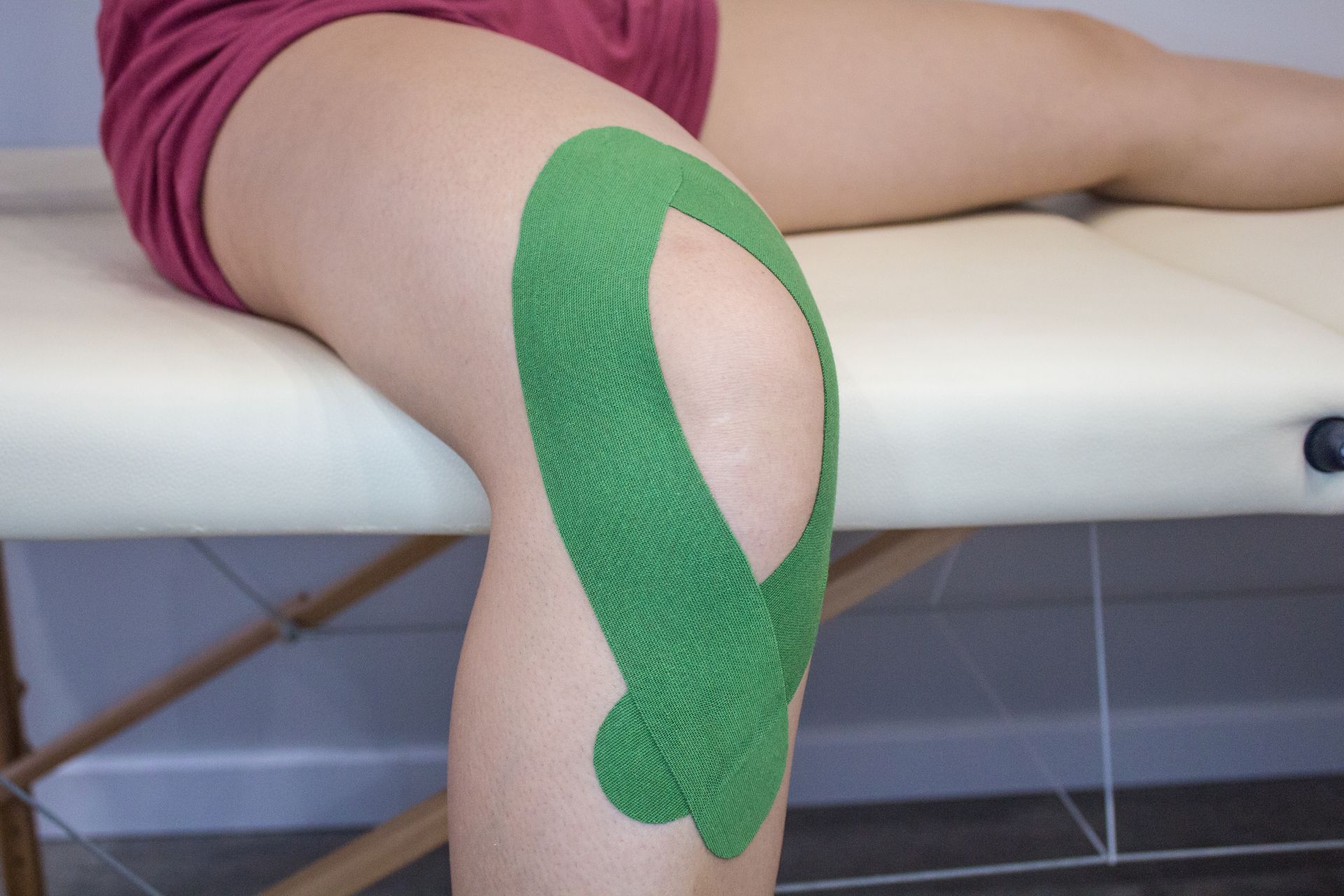 A close-up view of a knee with green kinesiology tape applied in a circular pattern around the kneecap.