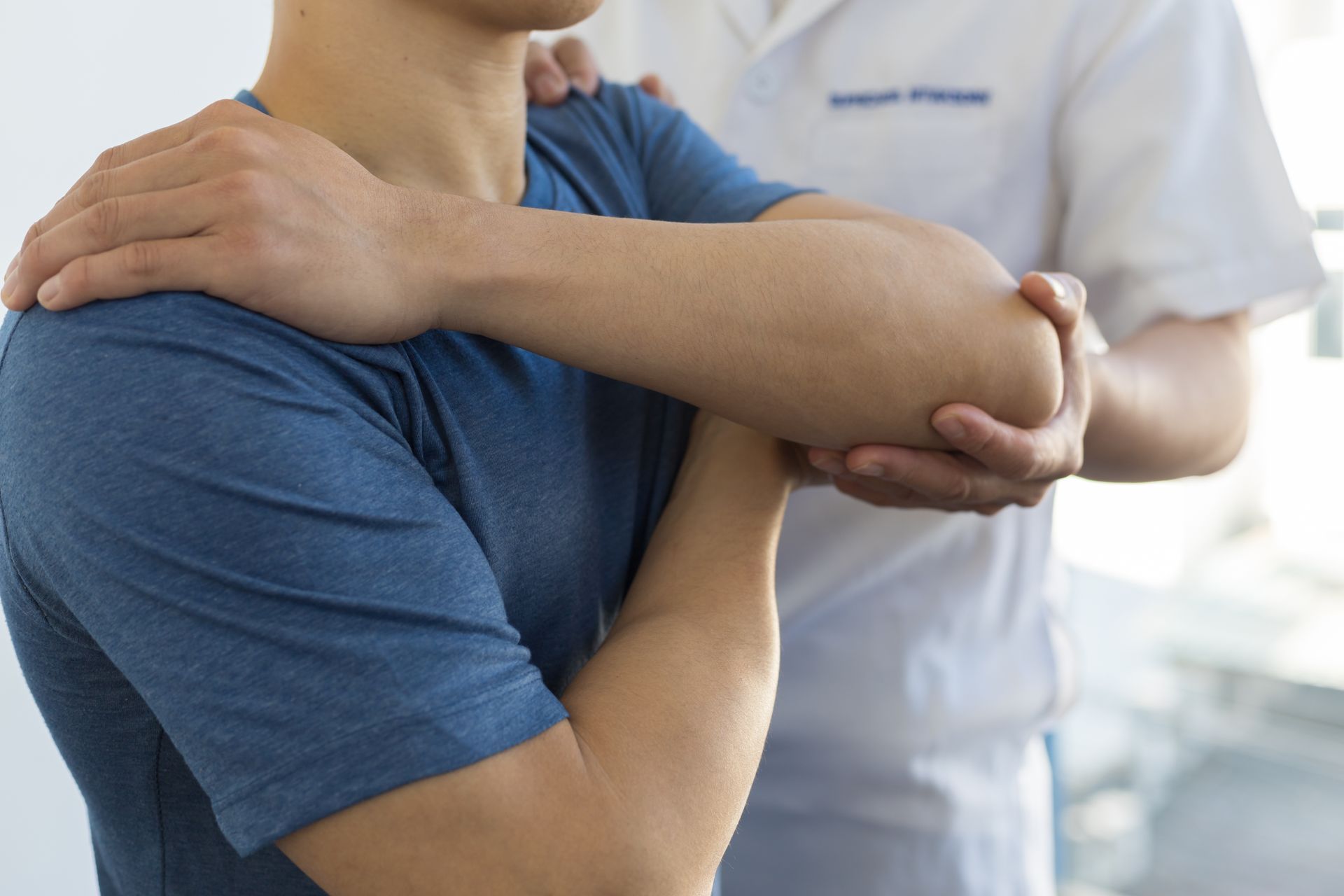 Person's arm being moved by another person, possibly physical therapy. Indoor setting, light skin tones.