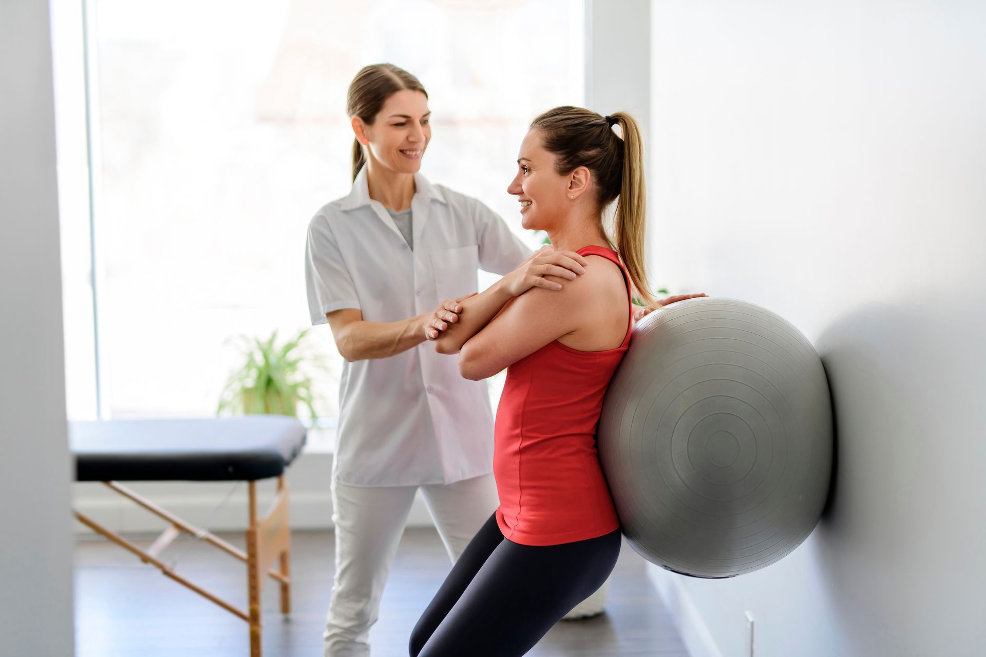 Woman doing wall squat with ball, guided by a healthcare professional.