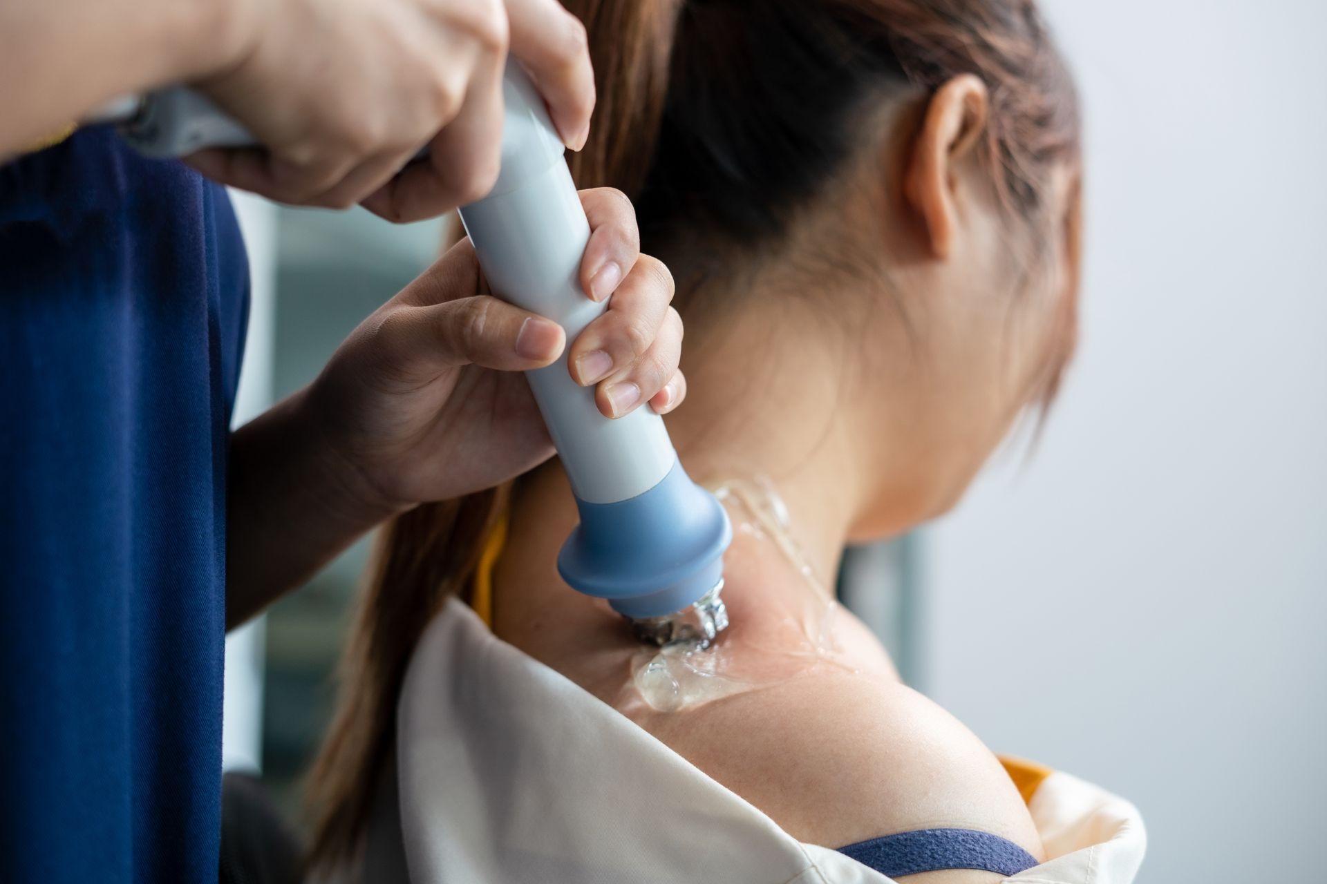 A person receiving a shoulder treatment with a handheld device, in a medical setting.
