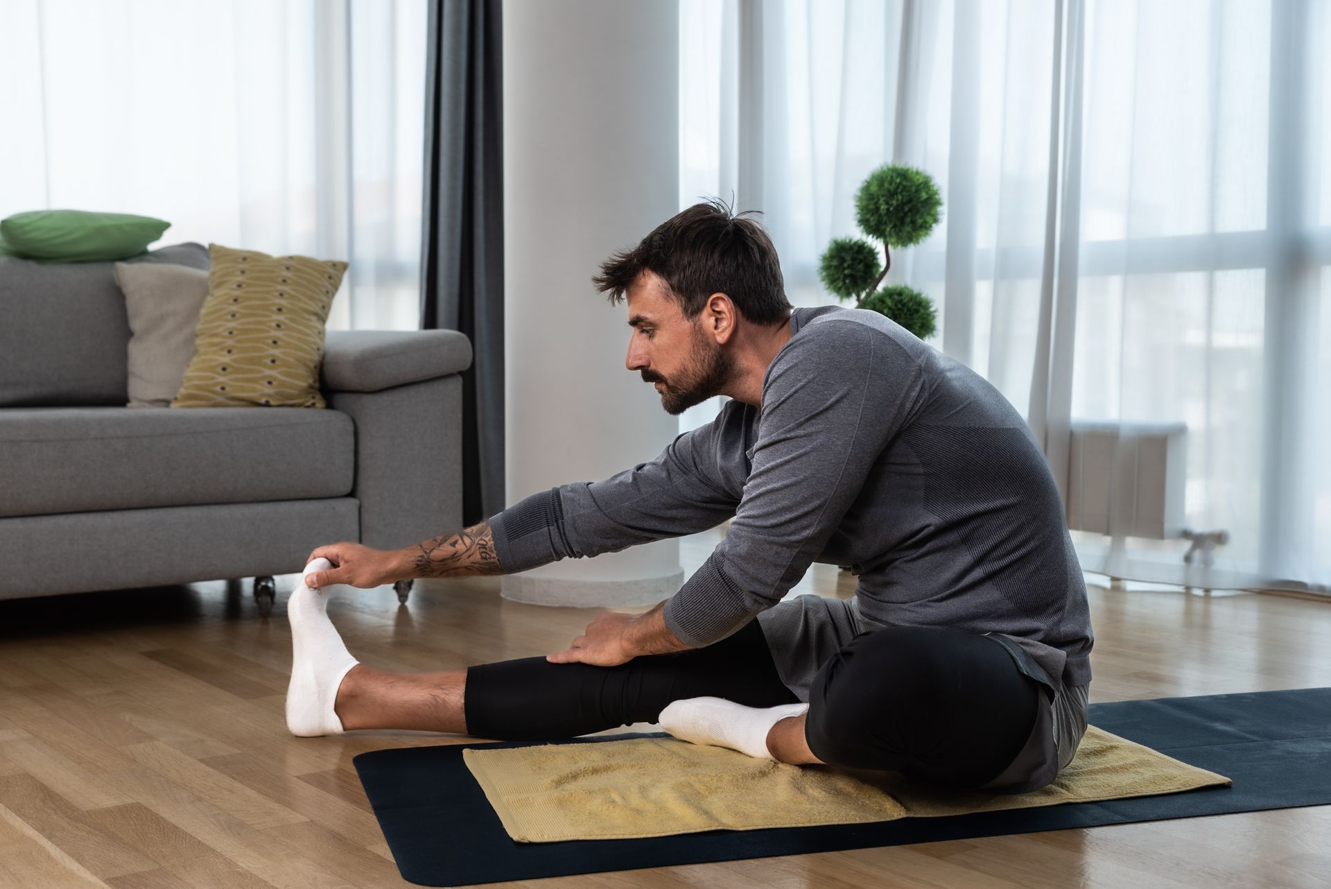 Man in grey shirt stretching leg on a mat indoors.