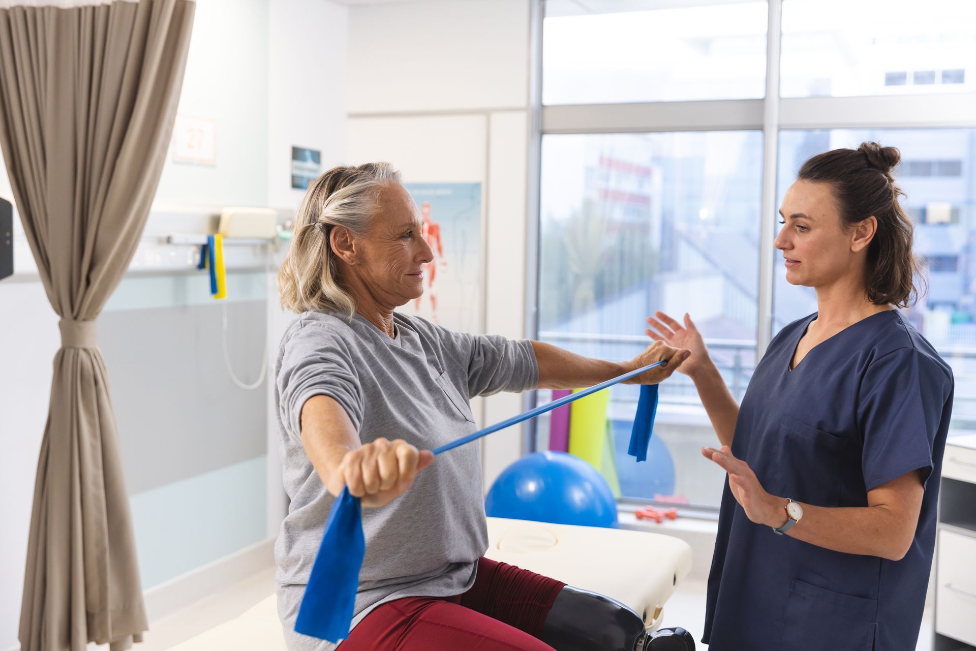 Therapist assisting a patient with resistance band exercises in a clinic setting.