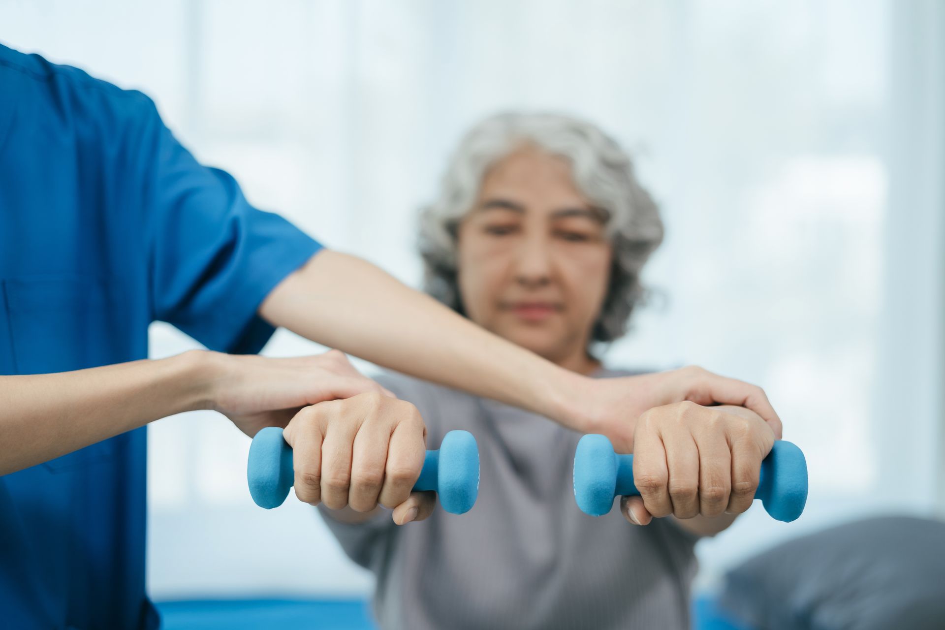 Therapist assisting a person with holding blue dumbbells in a home setting.