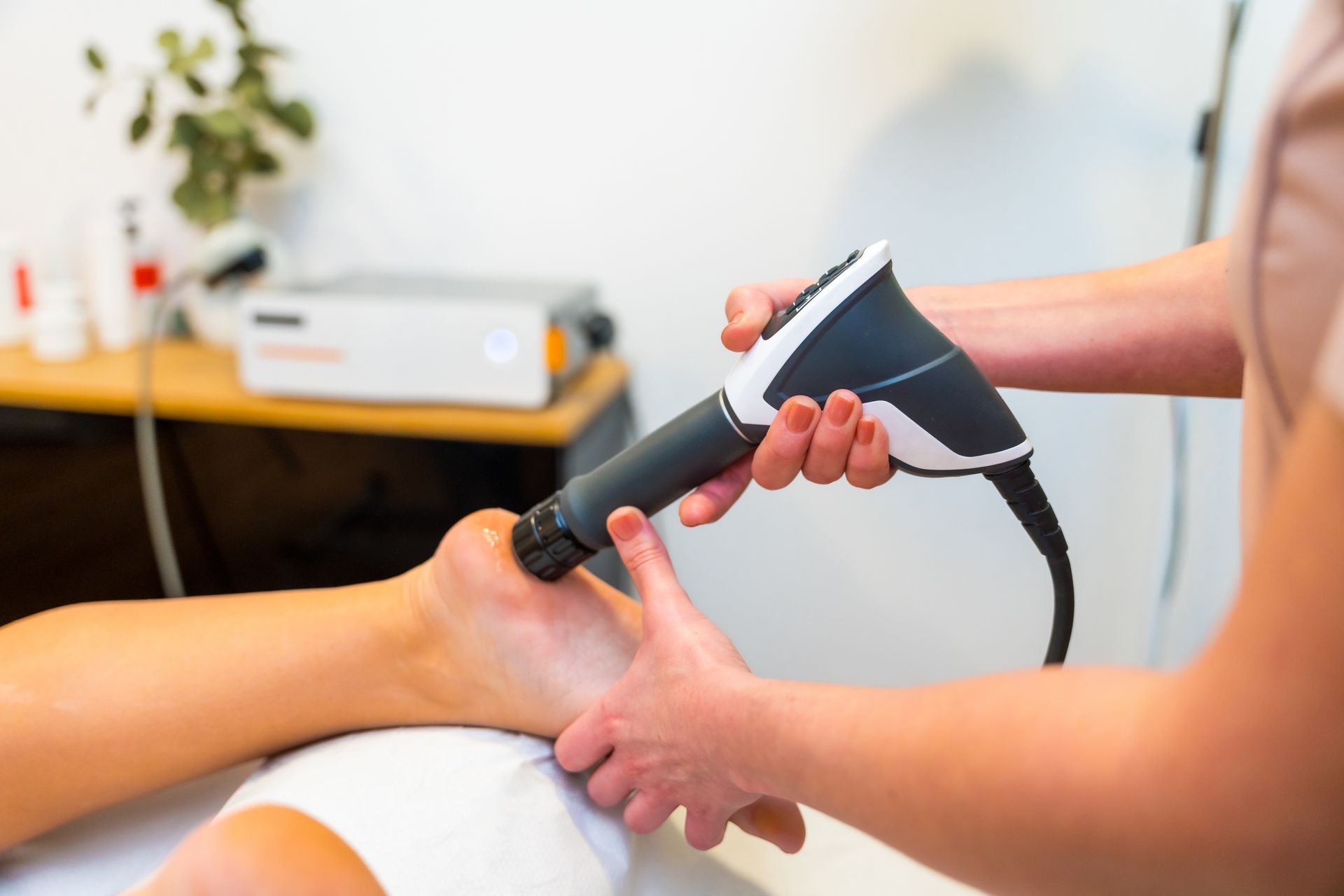 A person receives shockwave therapy on their ankle. A therapist holds the device.