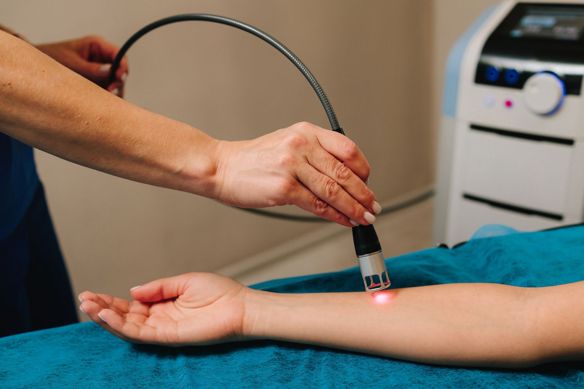 A practitioner uses a laser treatment wand on a person's forearm in a clinical setting.