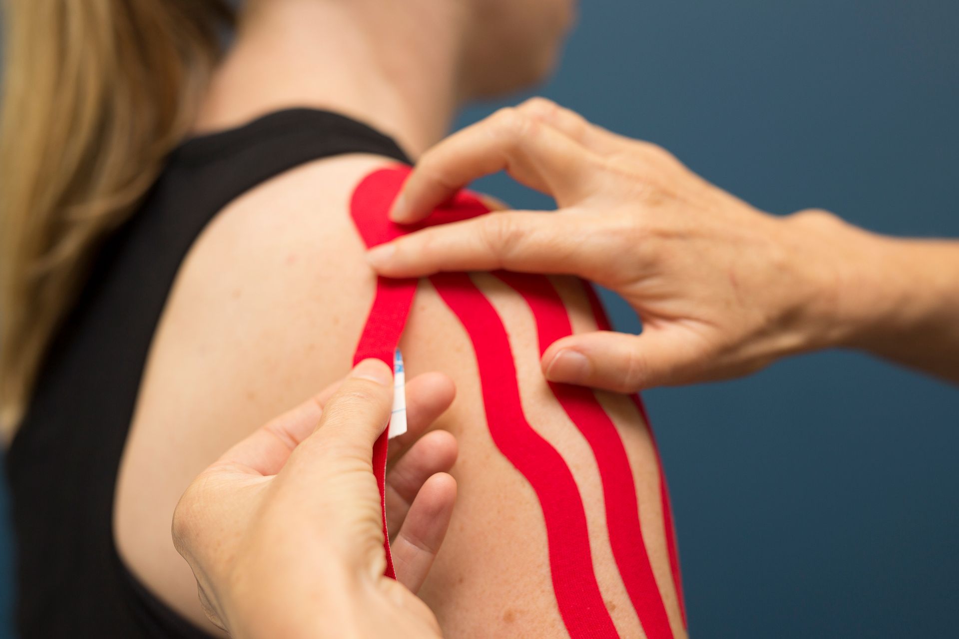 A person receiving red kinesiology tape on their shoulder.